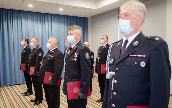 Zdjęcie przedstawia przedstawicieli OSP którym wręczono symboliczne promesy. Wszyscy w mundurach i maseczkach ochronnych.